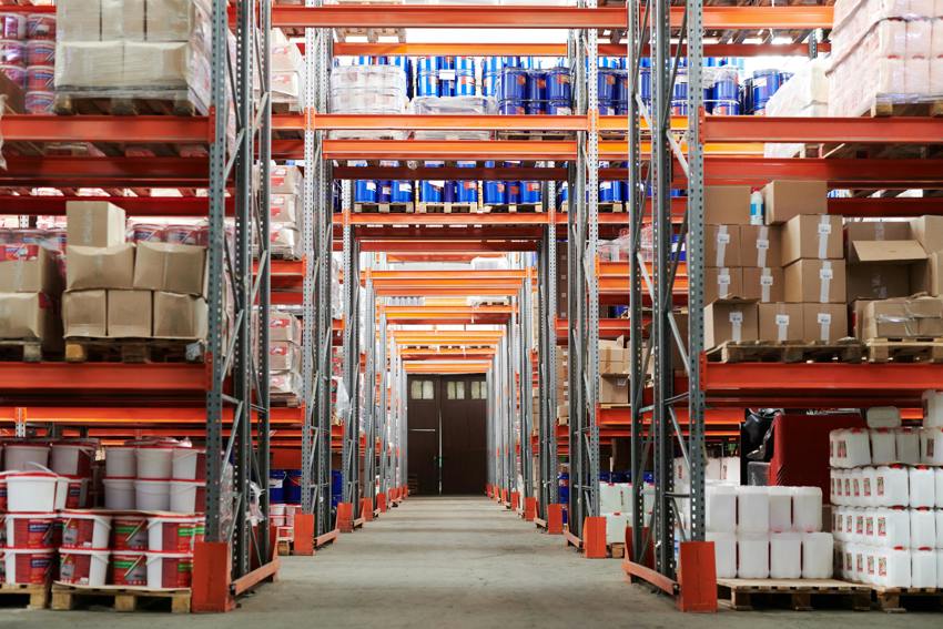 An image of a warehouse aisle with full shelves on either side and a door at the end of the aisle