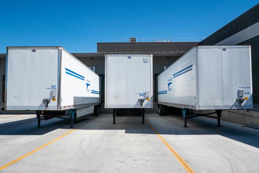 An image of three white delivery trucks from the rear, parked outside a warehouse.