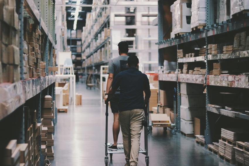 A man and a woman walking down a warehouse aisle with a trolley